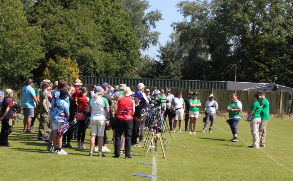 A group of gathered archers from various clubs listening to the tournament officer and judges.